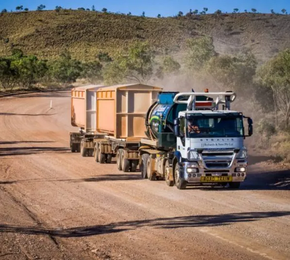 Heavy-duty road train transporting large waste and recycling containers along an unsealed mining